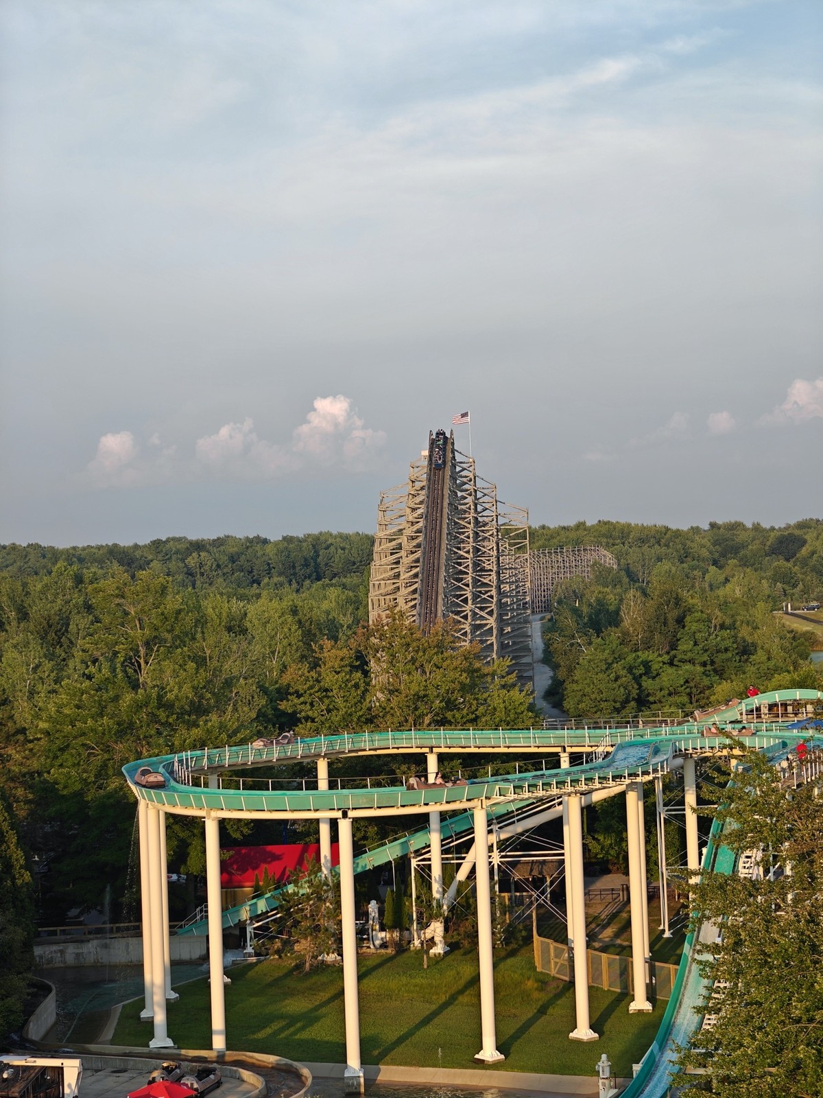 A rollercoaster car creating the lift hill with the tracks nearly squarely framed in the photo. A log flume is in the foreground.