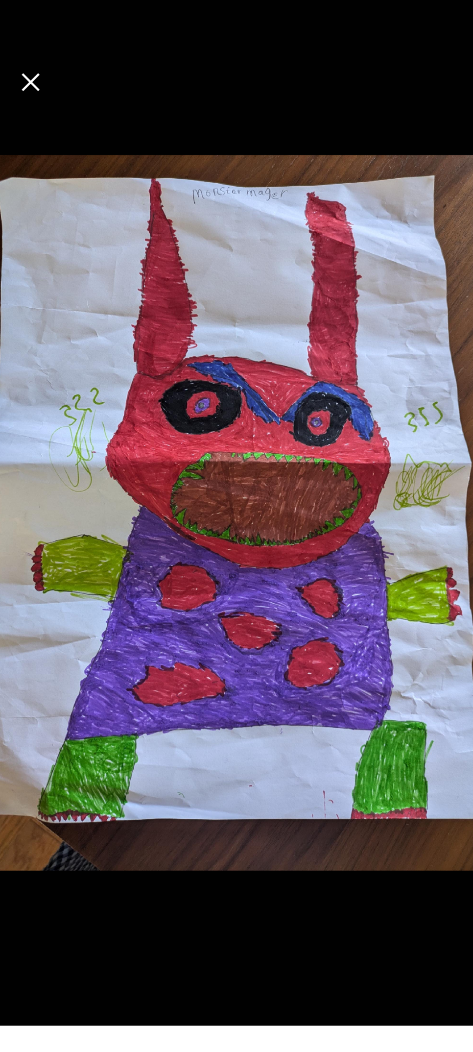 A child's drawing of a scary monster. It has a square purple body with five large red spots in the middle, stubby green arms and legs with red claws and a big round red head with tall ears, one pointed, the other more square, big black eyes with blue pupils and thick, frowning blue eyebrows. It also has a large wide open oval mouth surrounded with small, sharp green teeth.