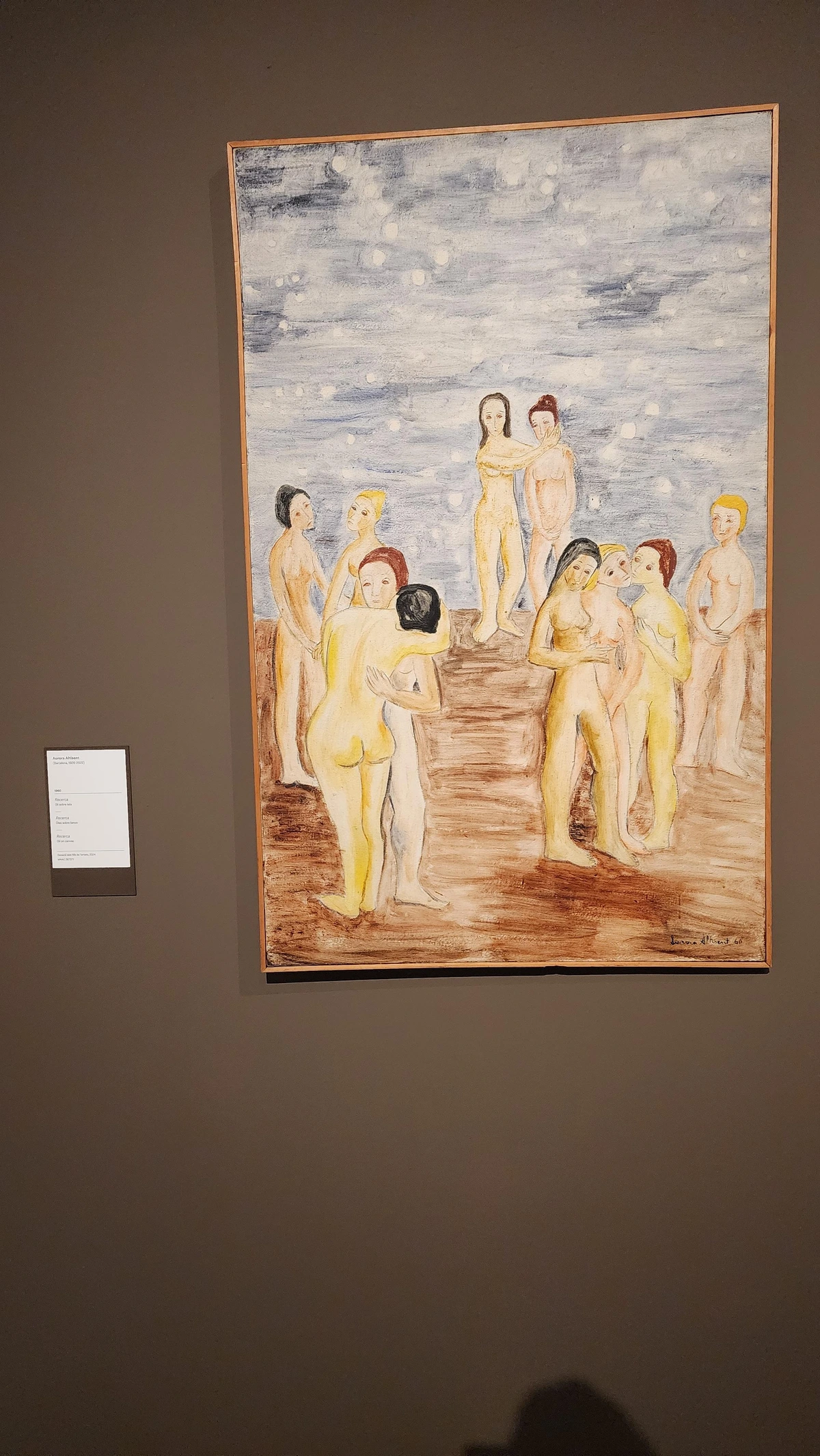 A large vertical canvas depicting roughly ten nude female figures gathered on a flat, rust-brown earth. Rendered in simplified, flattened forms with warm ochre and yellow skin tones, the figures stand, turn, and converse in loose groupings — some face away, some embrace, some look outward. At center, two figures stand slightly elevated, as if on a low step, facing the viewer. The sky filling the upper half is pale blue-grey, animated by scattered white circular orbs — ambiguous as stars, snowflakes, or luminous bubbles. The mood is contemplative and mythic. Signed lower right: Aurora Altisent 60.